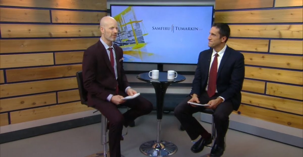 John Scholes, host of the Employment Law Show sits on a stool next to Employment Lawyer Lior Samfiru, Co-founding Partner at Samfiru Tumarkin LLP, with a coffee table and large flat screen TV between them, on the set of the well-known legal television show.