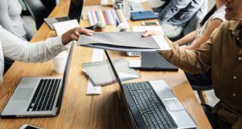 Computers and Reports on Table Amid Meeting Professionals