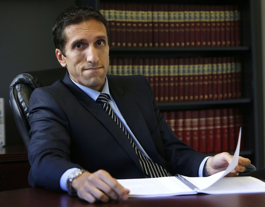 Employment Lawyer Lior Samfiru, Co-founding Partner at Samfiru Tumarkin LLP, sits at a cherry red wooden table with an open binder, leaning back in a leather chair positioned in front of a large legal bookcase, looking confidently at the camera.