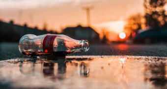 An empty bottle of coke lies on the pavement as the sun sets behind it. Coca-Cola employees are entitled to severance packages.