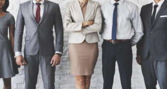 Five well-dressed disability lawyers, three male and two female, are lined up in front of a wall, striking various confident poses.