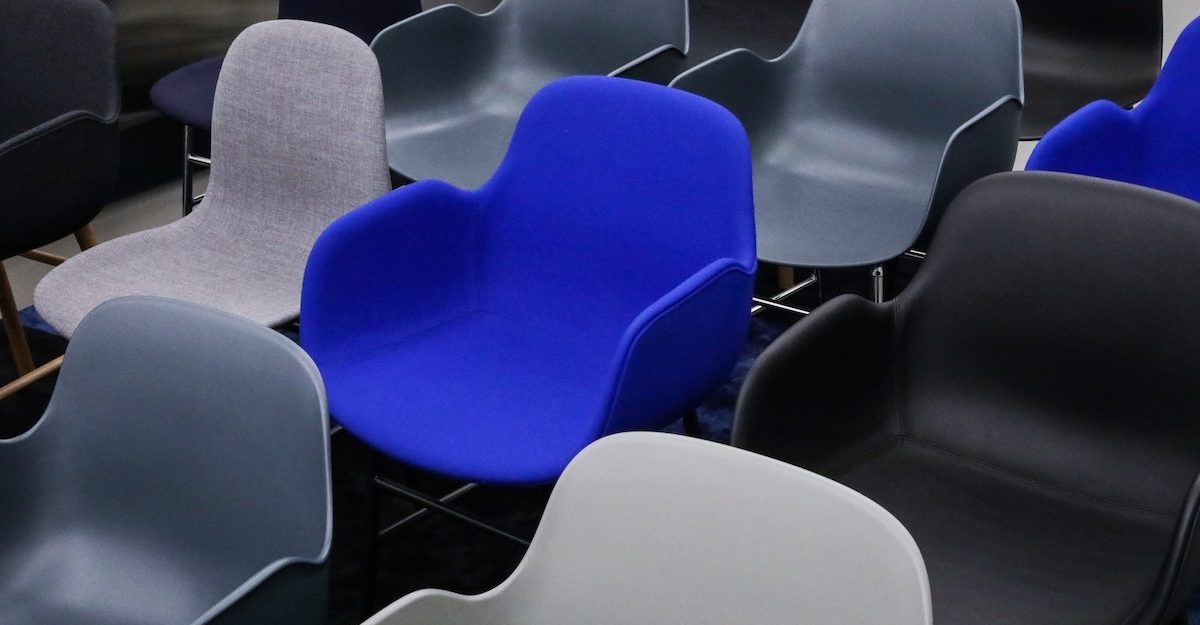 A blue chair is surrounded by grey chairs. Article owes severance pay to its fired employees.