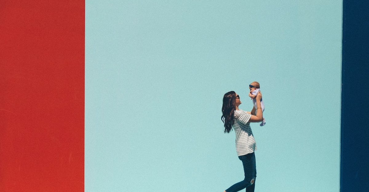 A young mother holds her baby in the air as she walks.