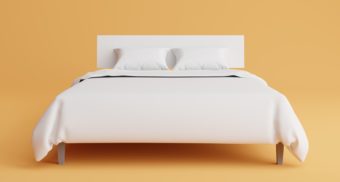 A white, neatly made bed rests on a light orange floor, against an equally orange background. Sleep Country Canada employees are entitled to full severance when they lose their job.