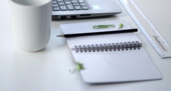 A cup of coffee next to a laptop and a notebook with a pen. Allstate Canada owes severance pay to employees who lose their job.