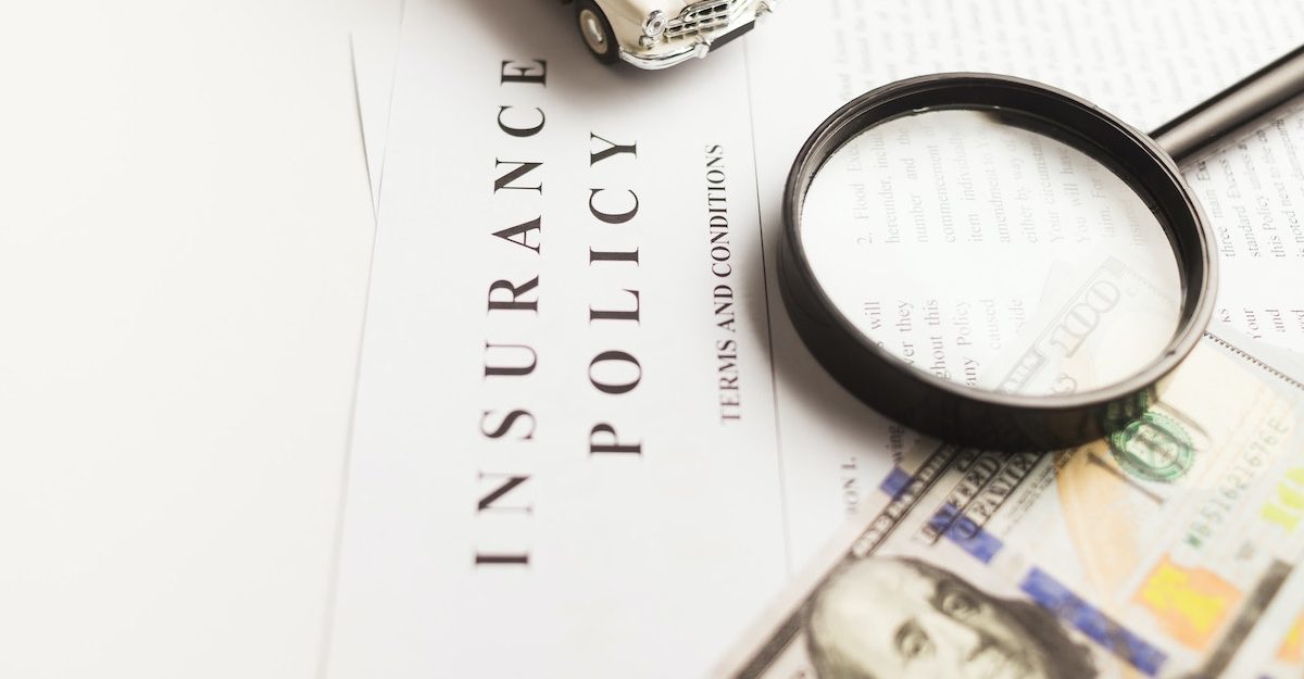 A magnifying glass, toy car and American money sit on top of a stack of papers titled 'Insurance Policy'. Manulife employees are entitled to severance when they lose their job.