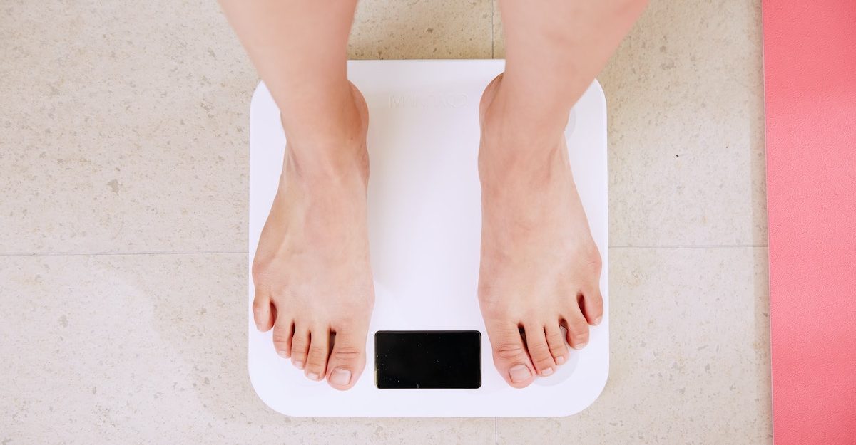 A bird's-eye view of someone's legs as the stand on a white bathroom scale. Jenny Craig employees are entitled to severance when they lose their job.