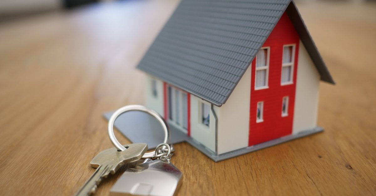 A key on a keychain lies next to a miniature house on a wooden table. Coldwell Banker employees get severance when they're fired from their job.