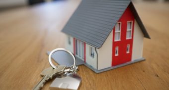 A key on a keychain lies next to a miniature house on a wooden table. Coldwell Banker employees get severance when they're fired from their job.