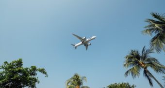 The belly of a passenger jet is seen flying over palm trees in a clear blue sky. Expedia Group employees are entitled to severance pay when they lose their job.