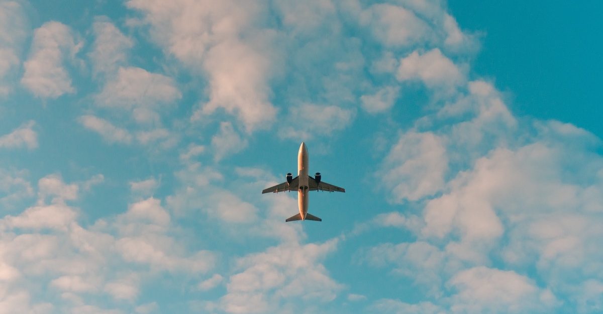 A view of an airliner's underbelly as it flies across a partly cloudy sky. Flight Centre employees are entitled to severance pay.