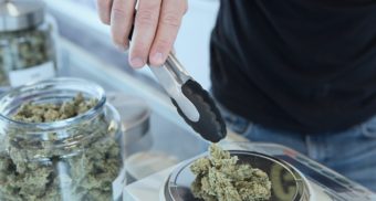 A cannabis store employee adds marijuana from a glass jar to a scale, using tongs. Pacific Smoke employees are entitled to severance pay when they lose their job.