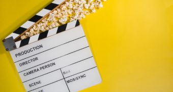 A traditional movie clapperboard lies flat on the ground with a handful of popcorn sitting in the agape clapper. Film and movie industry employees are entitled to severance pay.