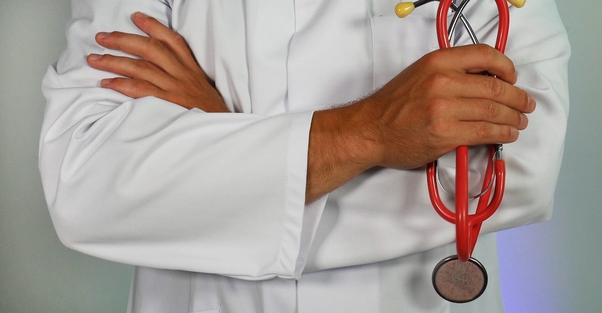 A doctor in a white lab coat stands with his arms crossed, with a stethoscope clutched in his right hand. Employees in the healthcare industry are entitled to severance pay.