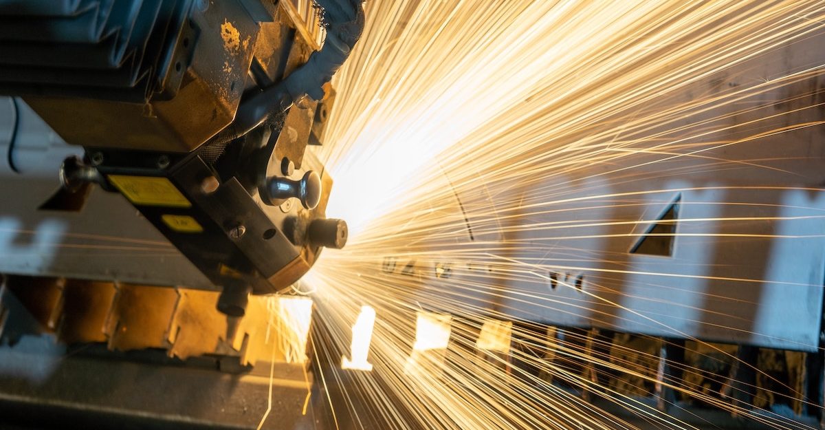 Sparks fly as a piece of equipment cuts holes into silver chunks of metal. Manufacturing sector employees are entitled to severance pay.