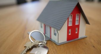 A set of keys sit on a wooden table next to a miniature model of a house. Real estate industry employees are entitled to severance pay.