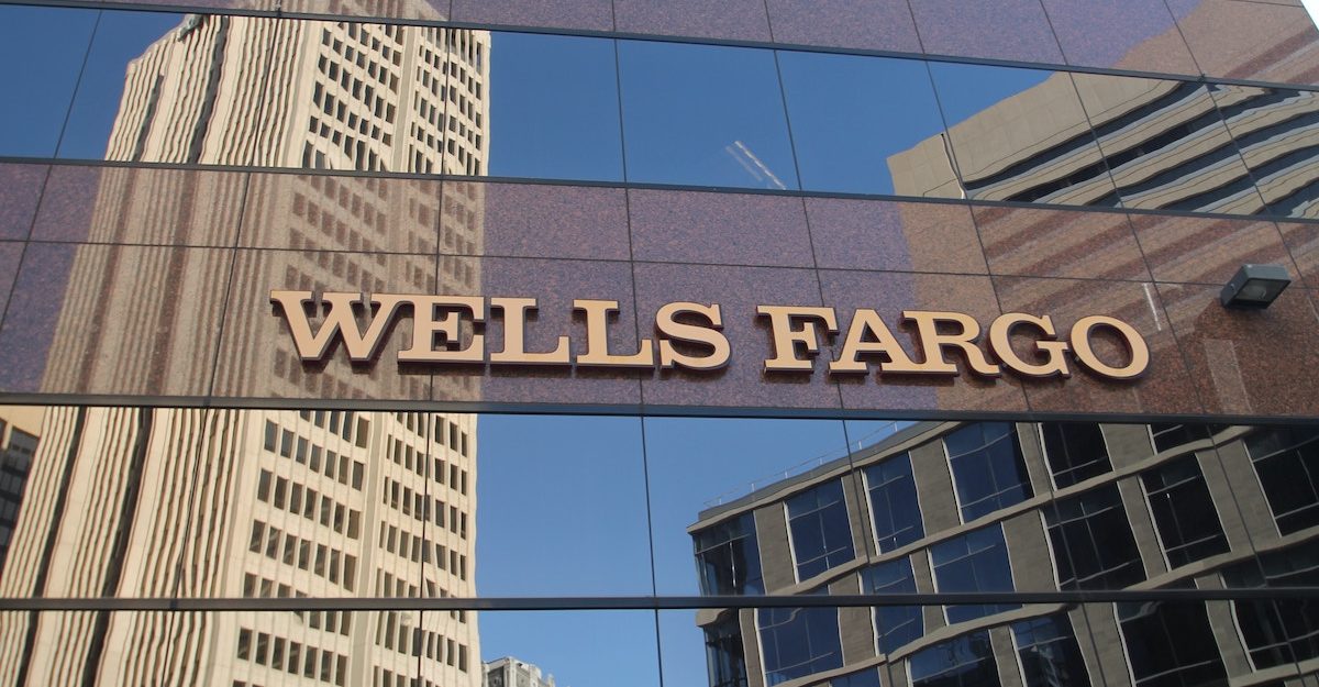 The Wells Fargo name is displayed on the side of an office building, with other skyscrapers reflected in the windows