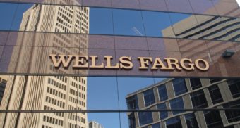 The Wells Fargo name is displayed on the side of an office building, with other skyscrapers reflected in the windows