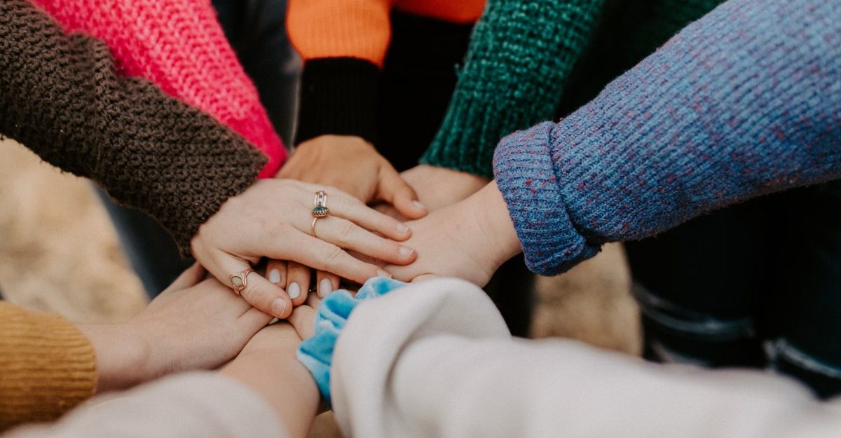 A photo of a group of people joining hands. (Photo: Hannah Busing / Unsplash)