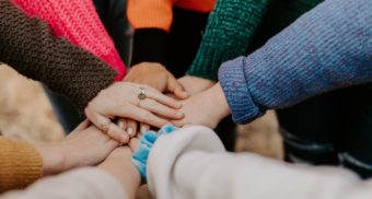 A photo of a group of people joining hands. (Photo: Hannah Busing / Unsplash)