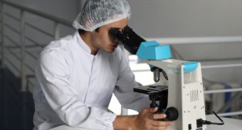 A medical professional examines something through a microscope. Lilly is buying Point Biopharma, potentially resulting in job loss and severance pay for some employees.