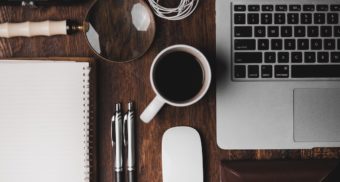 An assortment of items one needs to carry out their job, including papers, pens, coffee, and a computer.