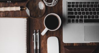 An assortment of items one needs to carry out their job, including papers, pens, coffee, and a computer.