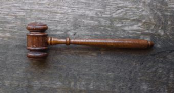 A photo of a brown gavel on a wooden table. (Photo: Wesley Tingey / Unsplash)