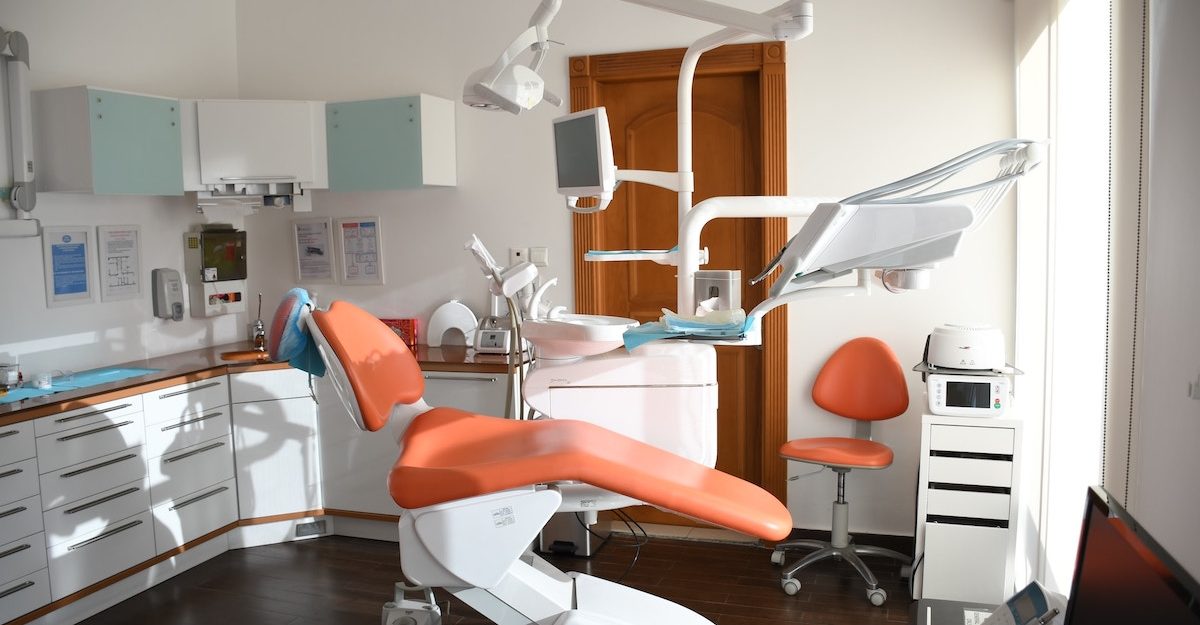 A dentist's chair sits in the middle of a neat and clean dental office.