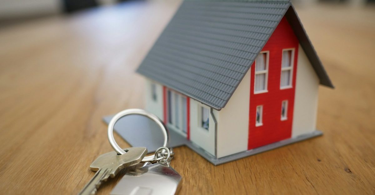 a key sits on a wooden table next to a miniature house, which may have been financed through MCAP.