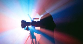 A photo of a person examining a camera in front of a projector. (Photo: Jakob Owens / Unsplash)