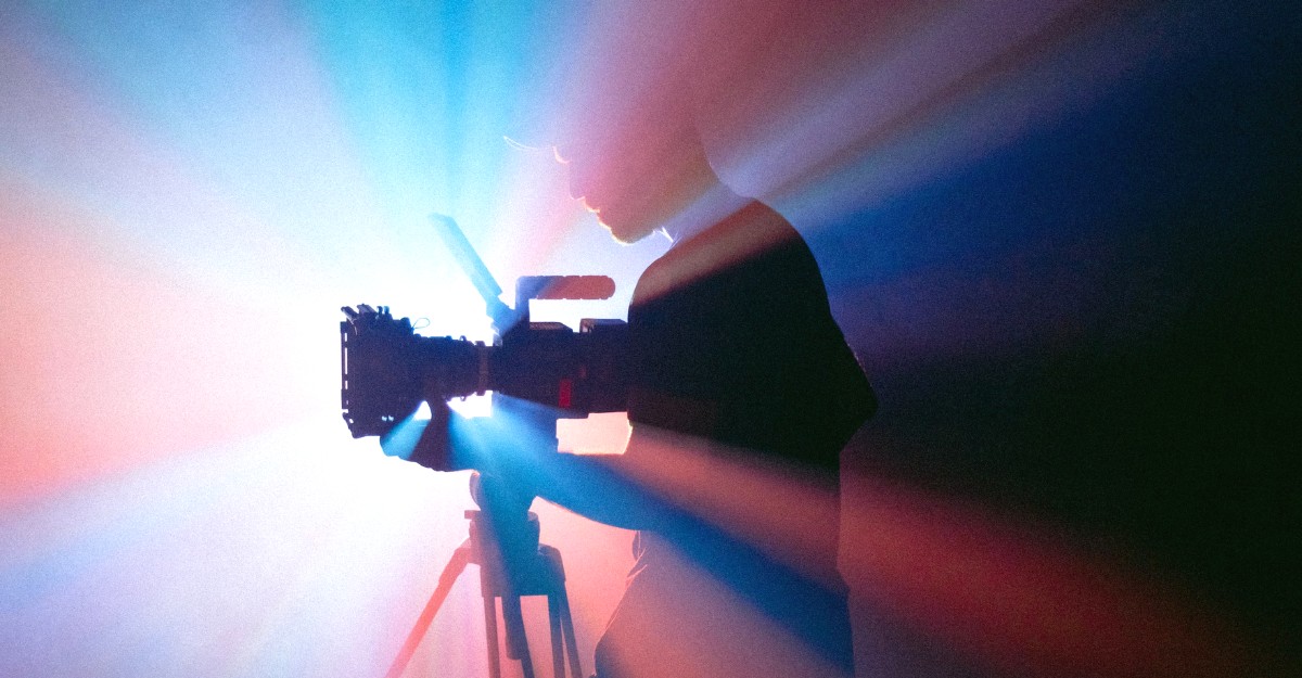 A photo of a person examining a camera in front of a projector. (Photo: Jakob Owens / Unsplash)