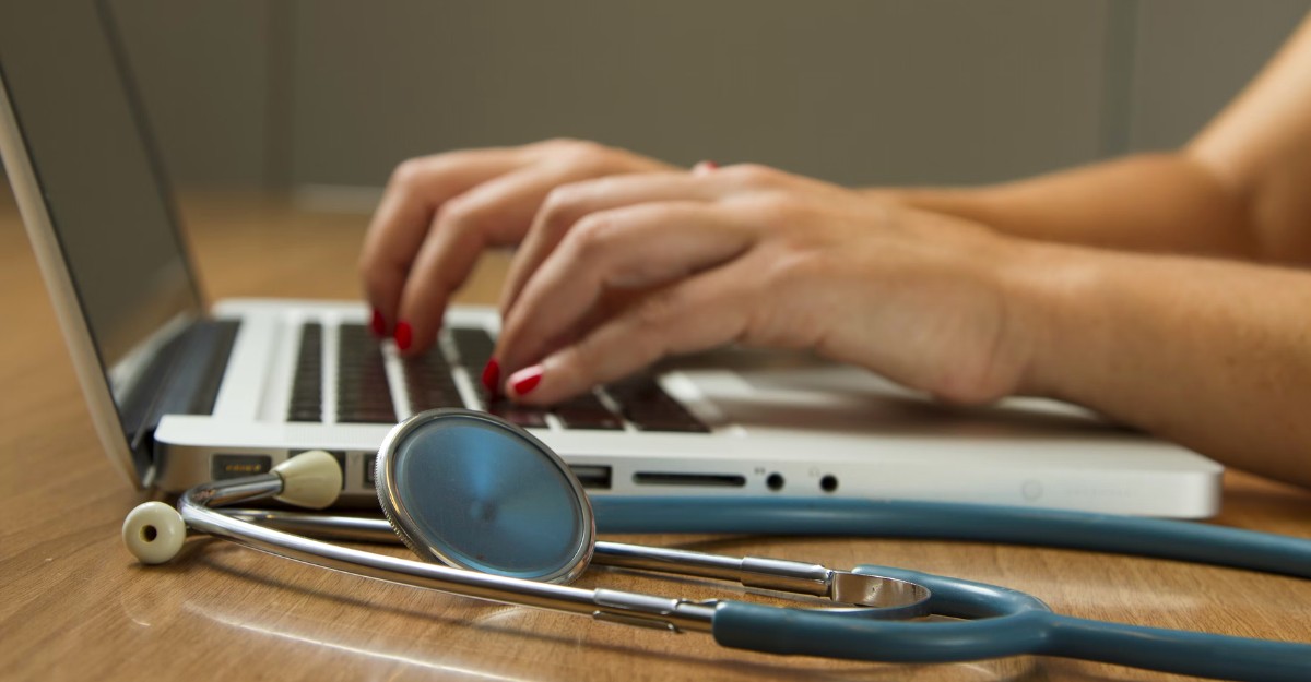 A photo of a person using a laptop with a stethoscope beside them. (Photo: National Cancer Institute / Unsplash)