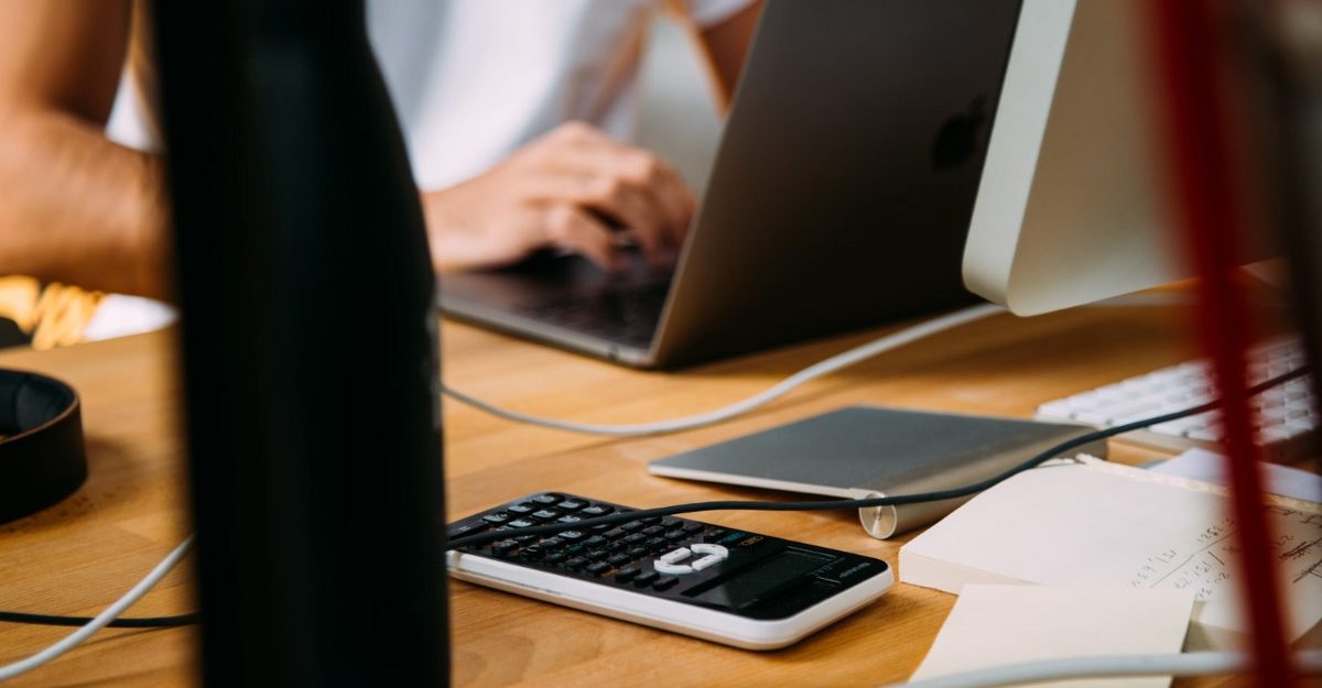 A photo of a person working at a desk covered in multiple items. (Photo: charlesdeluvio / Unsplash