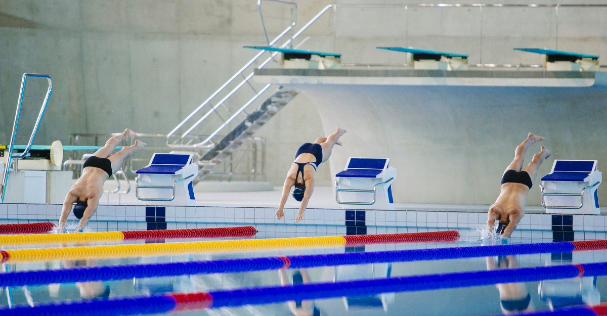 A photo of three people diving into an indoor swimming pool. (Photo: Dylan Nolte / Unsplash)