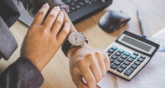 Employee checking their watch at a desk beside a calculator, symbolizing changed work hours in Ontario.