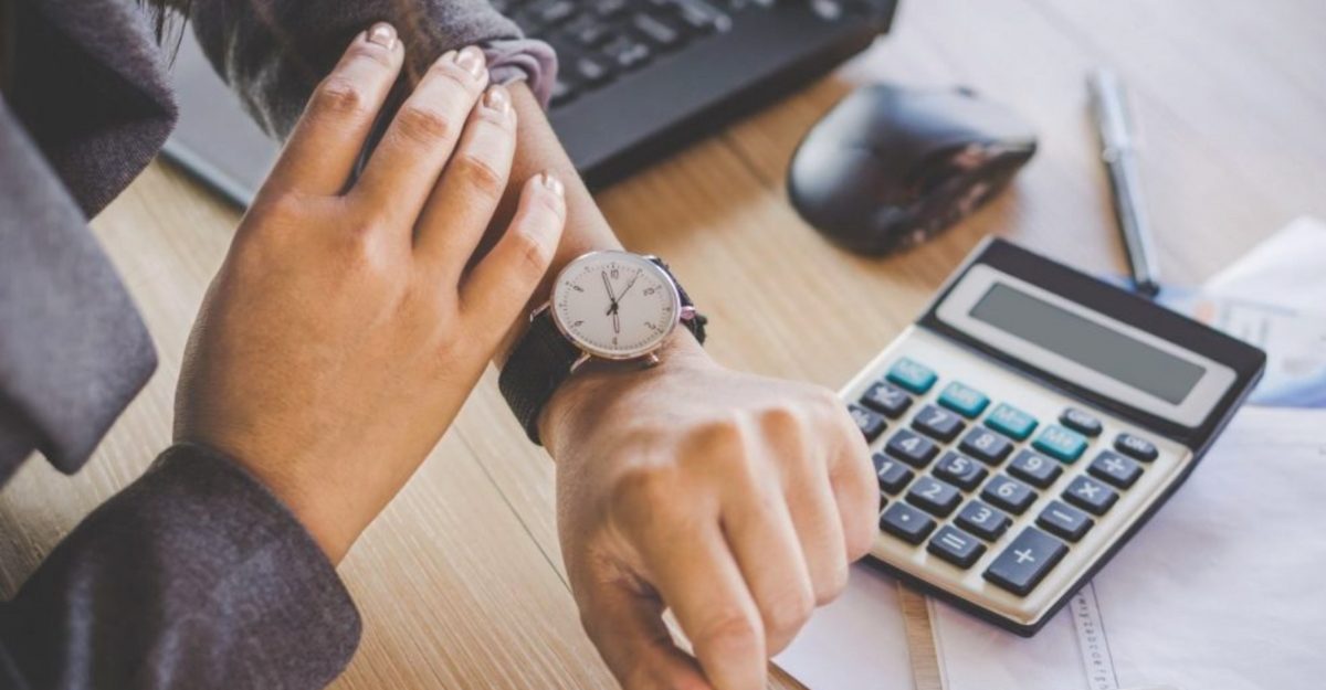 Employee checking their watch at a desk beside a calculator, symbolizing changed work hours in Ontario.
