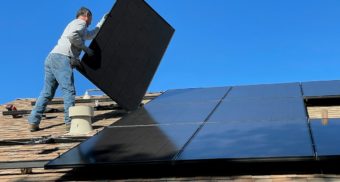 A solar panel installer works on a roof as part of Canada's Greener Homes program.