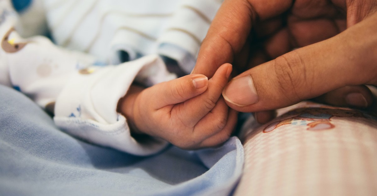 A photo of a person holding a baby's hand. (Photo: Aditya Romansa / Unsplash)