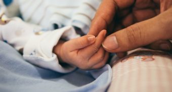 A mother holding her child's hand while on parental leave in Alberta.