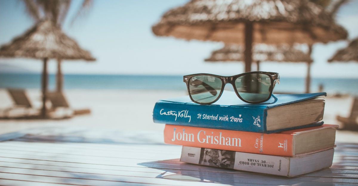 A pair of sunglasses rest on a stack of books near a tropical beach during vacation for a worker from Alberta.