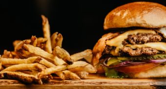 A photo of a burger and fries on a wooden table. (Photo: Jonathan Borba / Unsplash)