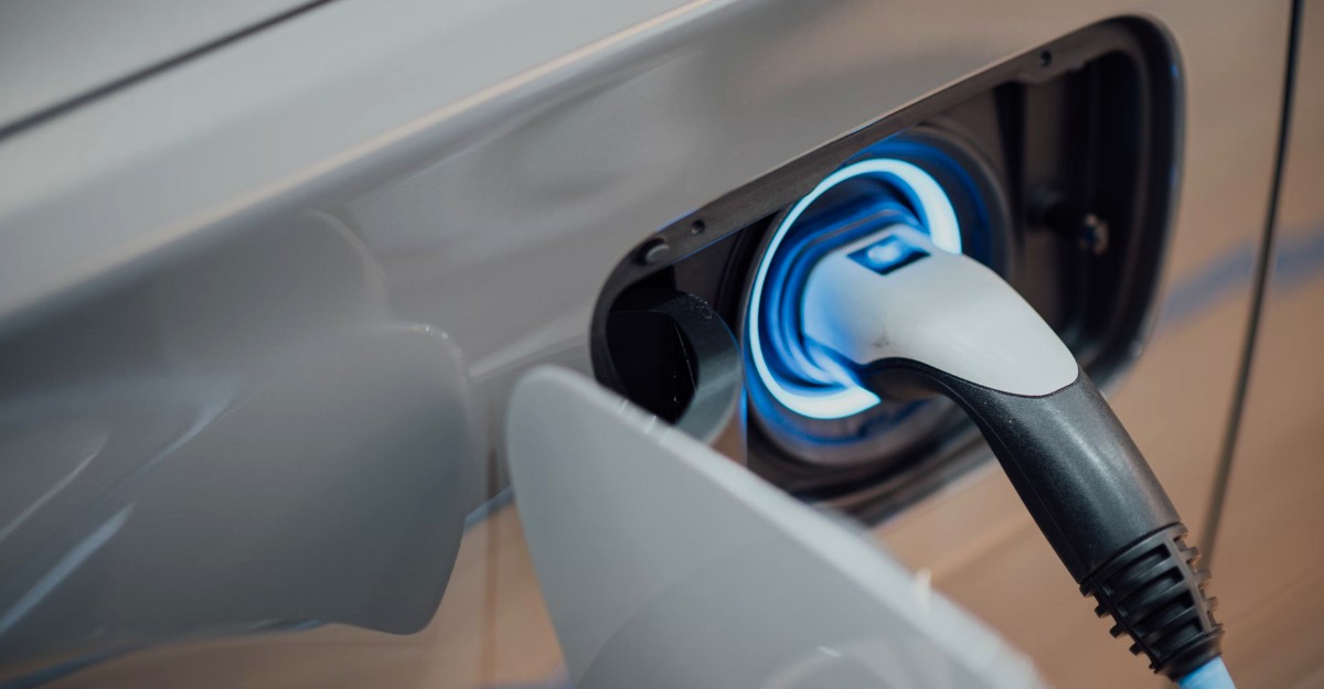 A photo of a person inserting a battery charger into an electric vehicle. (Photo: CHUTTERSNAP / Unsplash)