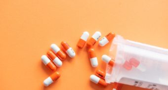 A photo of a dozen pills next to a pill bottle lying on its side, potentially a Bayer product.