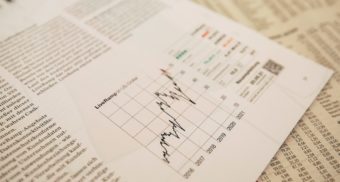 A sheet displaying financial information, possibly for Edward Jones, sits on top of the stock section of a newspaper.