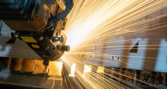 Sparks fly as a piece of equipment, potentially used by Active Dynamics, cuts holes into silver chunks of metal.