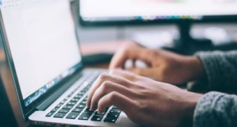 A close up of someone's hands hovering over a laptop keyboard, potentially working for DXC Technology.