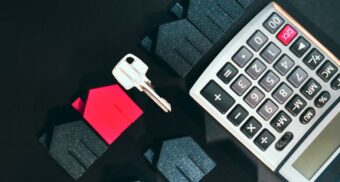 A photo of small houses, a key, calculator on a table. (Photo: Jakub Żerdzicki / Unsplash)