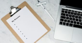 A blank resume lies on a table next to a pen and laptop, perhaps being drafted for review by Procom.