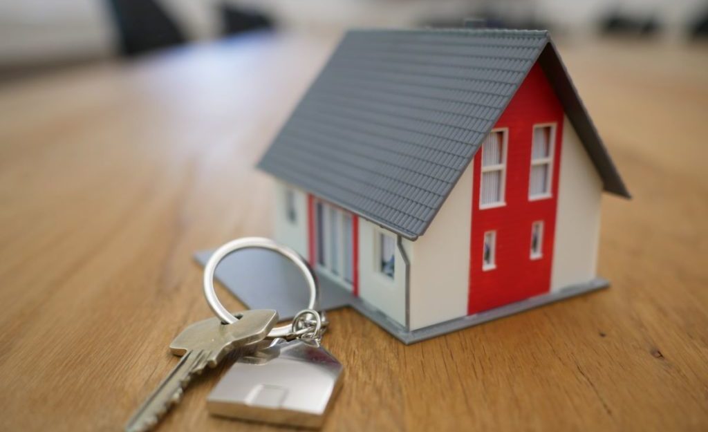 A set of keys sit on a wooden table next to a miniature model of a house. Property managers are entitled to severance pay.